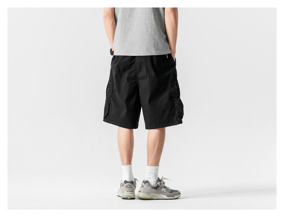 Back view of a model wearing black cargo shorts with flap pockets at the sides.
