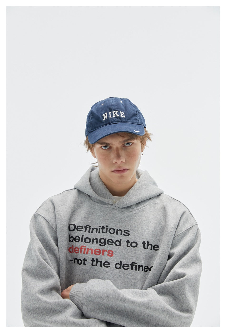 Close view of a model wearing a gray slogan-print hoodie and a blue embroidered cap.