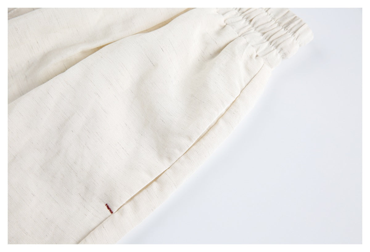 Close-up of an ivory shorts leg seam and hem with a small maroon stitched mark.