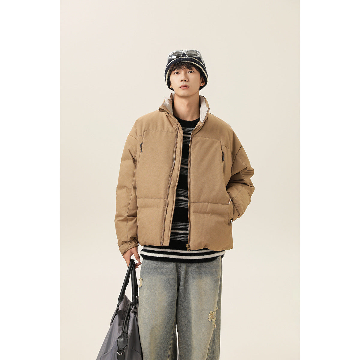 Model wearing an open tan padded jacket with a high collar, layered over a striped sweater.