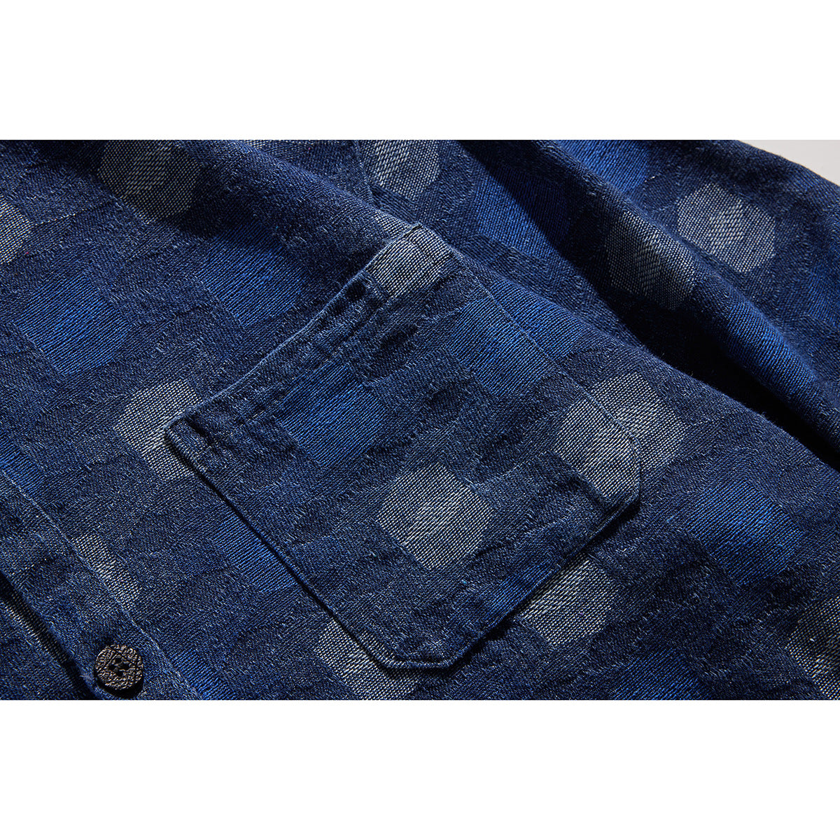 Close-up of a dark blue patterned shirt pocket, fabric, and dark button.