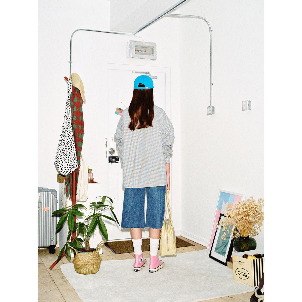 Back view of a model wearing a pale blue check button-up shirt, denim shorts and a bright blue cap.