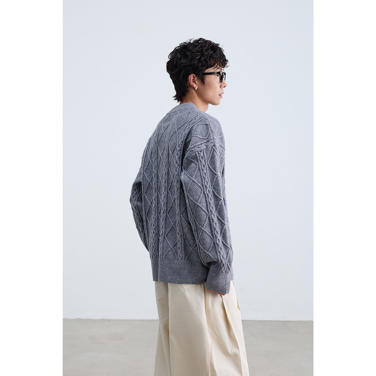 Side view of a model wearing a gray cable-knit sweater with diamond panels and ribbed cuffs and hem.