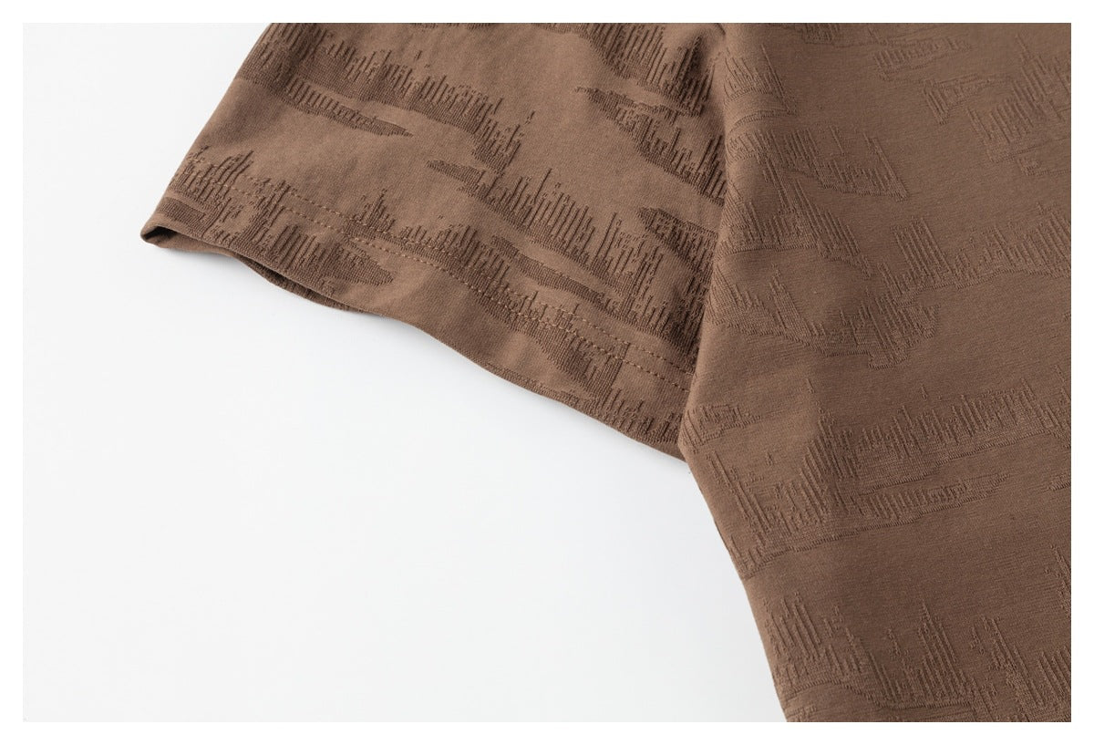 Close-up of a brown T-shirt sleeve and body, showing the raised geometric texture and sleeve hem.