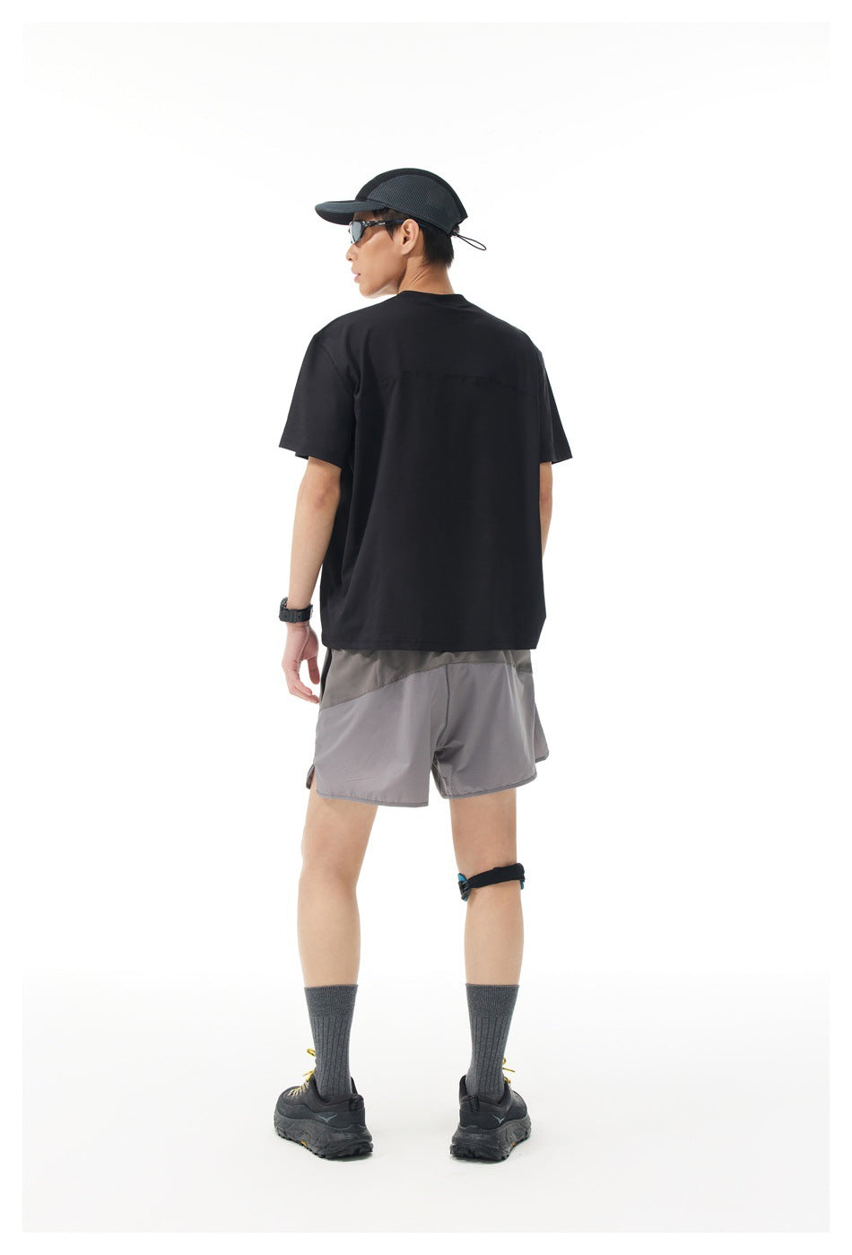 Rear view of a model wearing a black short-sleeve shirt and gray athletic shorts.