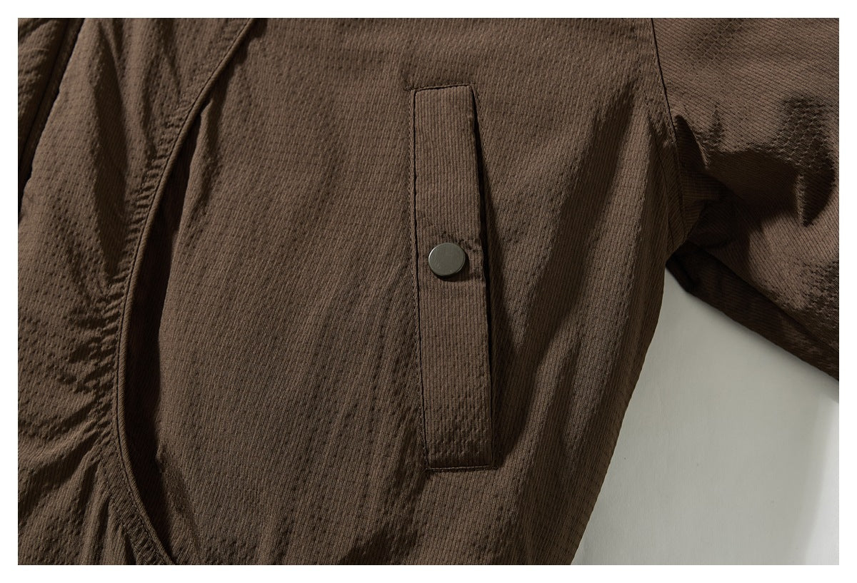 Close-up of a dark brown jacket's vertical pocket flap with a dark snap button.