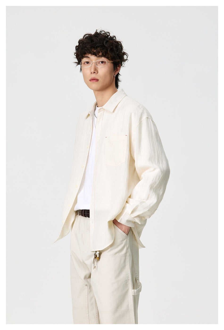 Model in a relaxed ivory button-up shirt with a single chest pocket, white tee, and cream trousers.