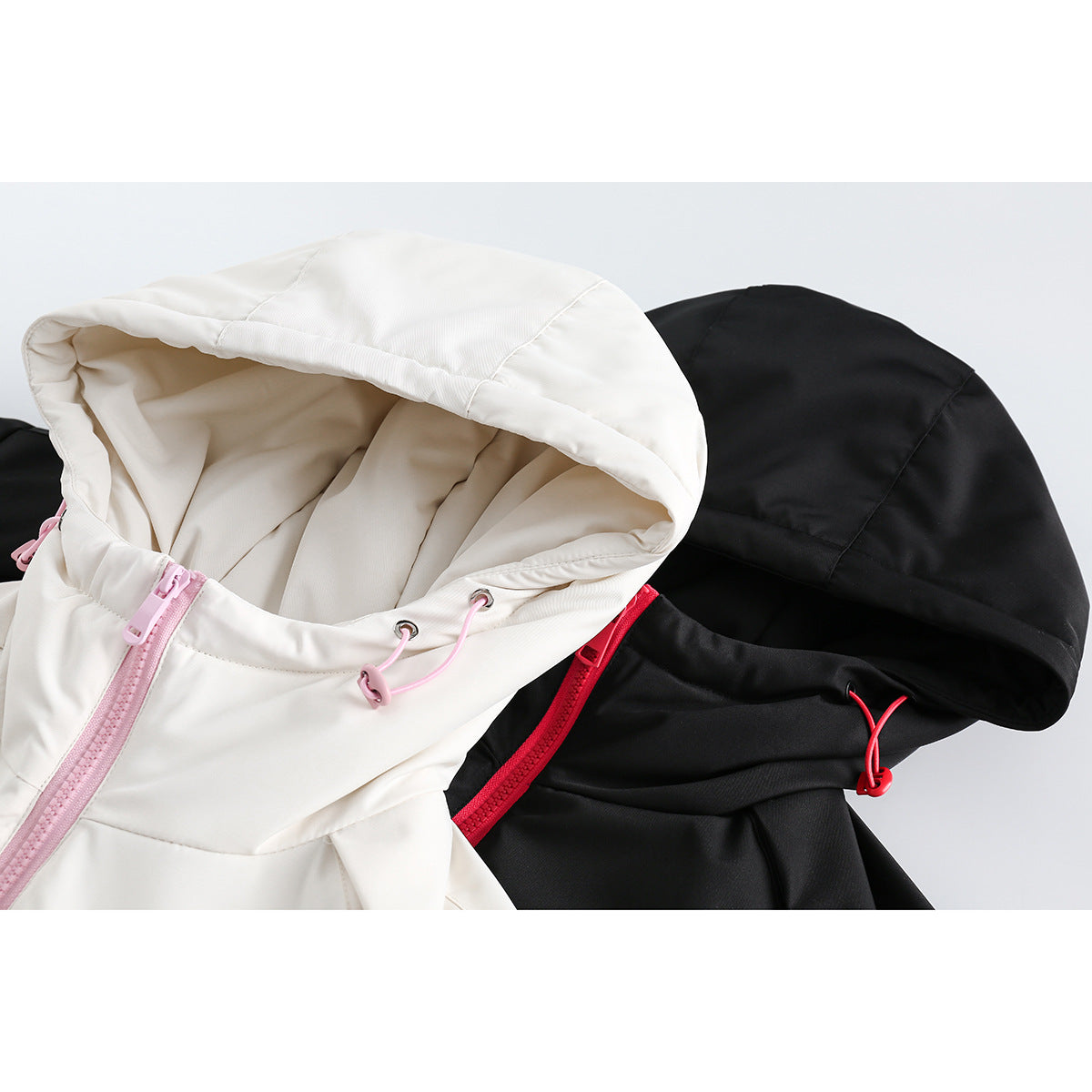 Close-up of white and black hooded jackets showing pink and red zippers and adjustable hood cords.