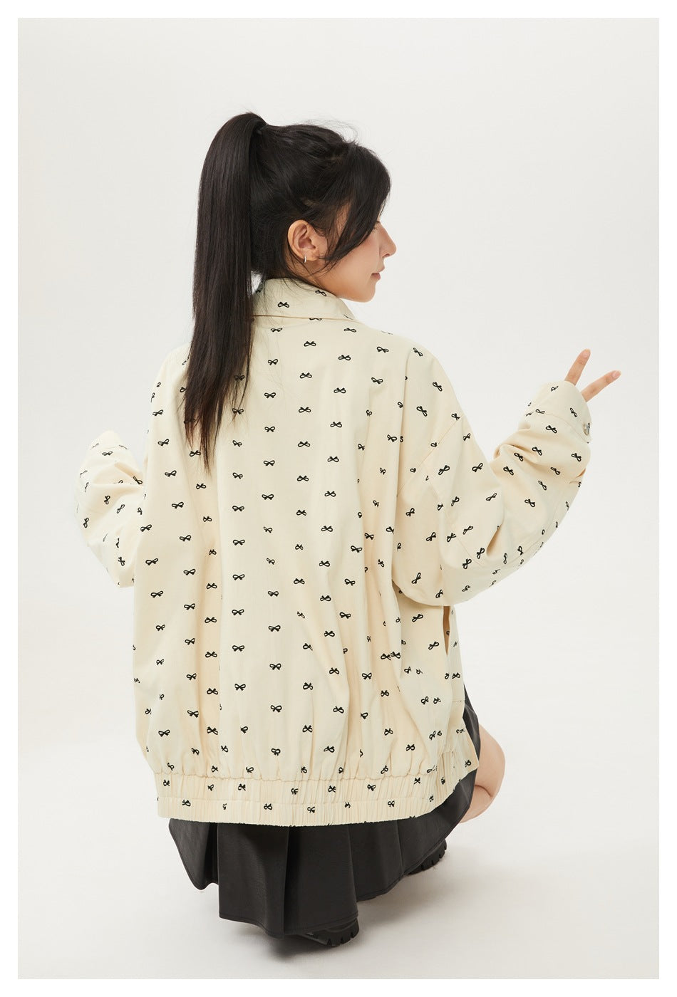 Model wearing a cream jacket with small black bow motifs, elastic hem and cuffs, shown from the back and side.