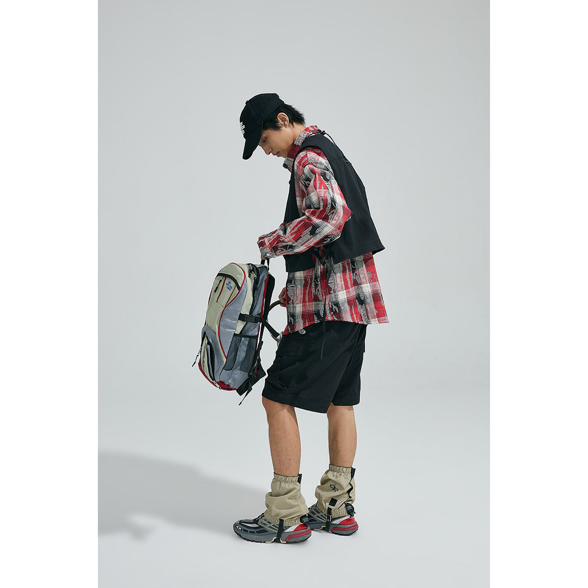 Side and rear view of a model wearing a black utility vest over a red plaid shirt.