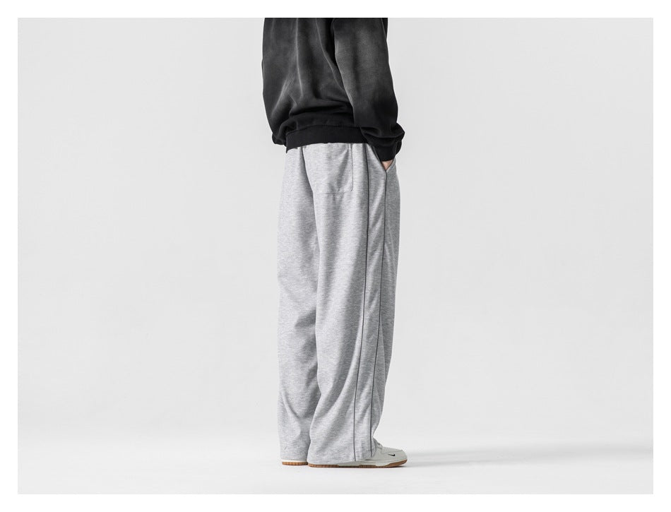 Rear-side view of a model wearing light gray wide-leg pants with dark piping and a back pocket.