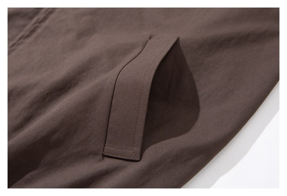 Close-up of a stitched pocket opening on dark brown fabric.