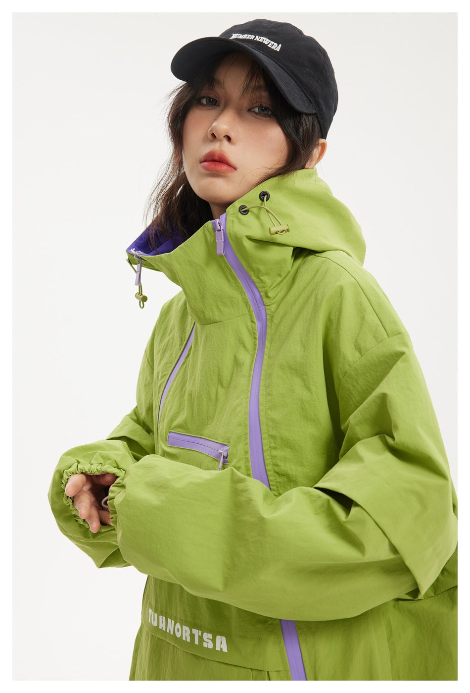 Close-up of a model in a lime green jacket, showing its high adjustable hood and lavender zipper details.