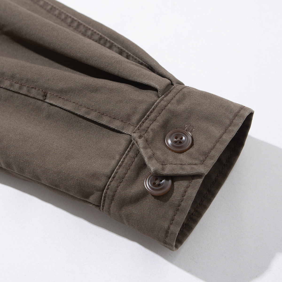 Close-up of a brown-gray jacket cuff with two brown buttons and visible topstitching.