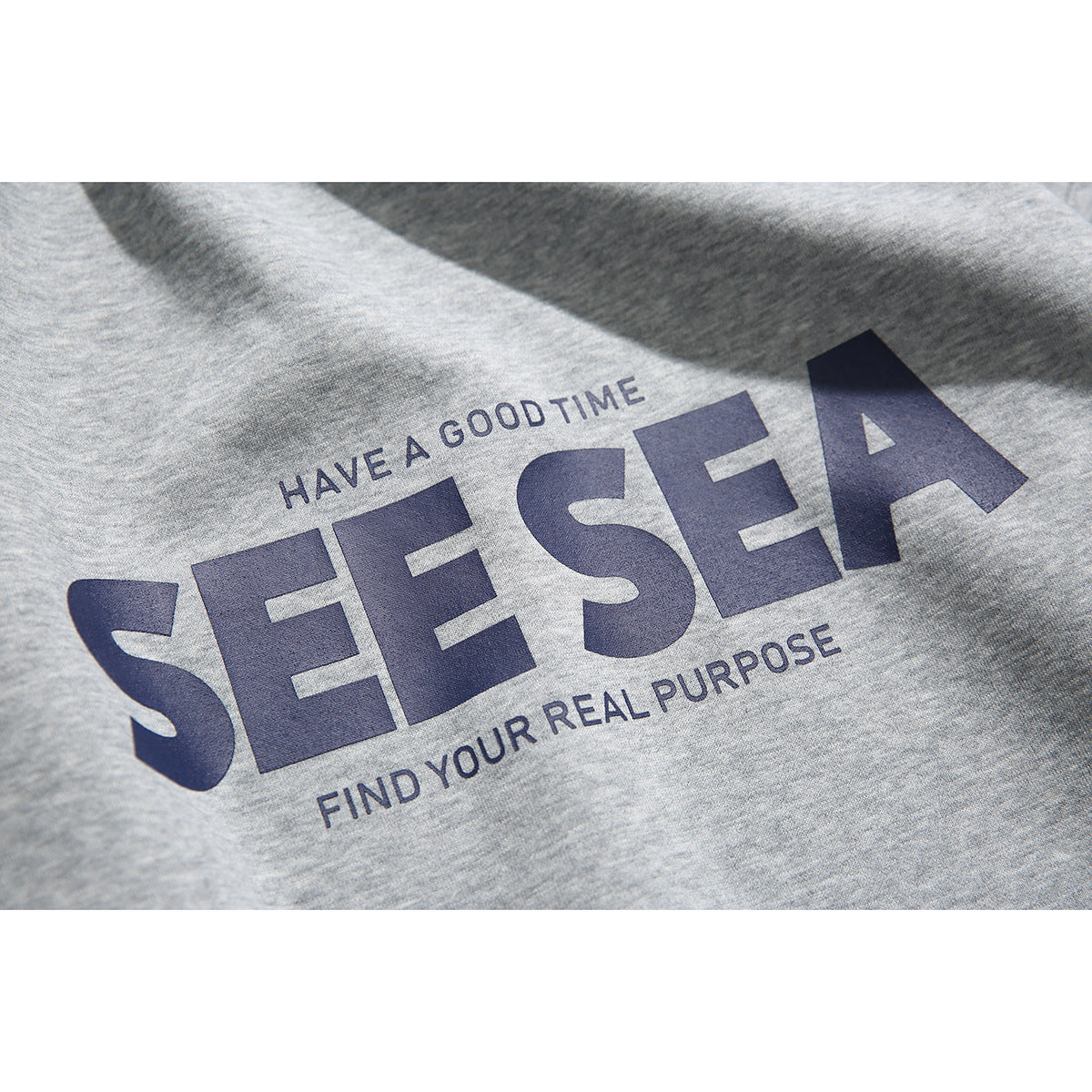 Close-up of the navy “SEE SEA” chest print on heather gray sweatshirt fabric.