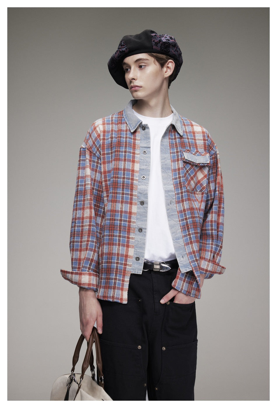 Model wearing an open blue, rust and cream plaid overshirt with a pale collar and chest pocket, shown with black trousers.
