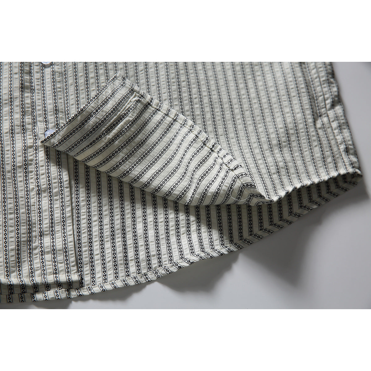 Close-up of the shirt's hem and folded fabric, showing its light ground and black geometric stripe pattern.