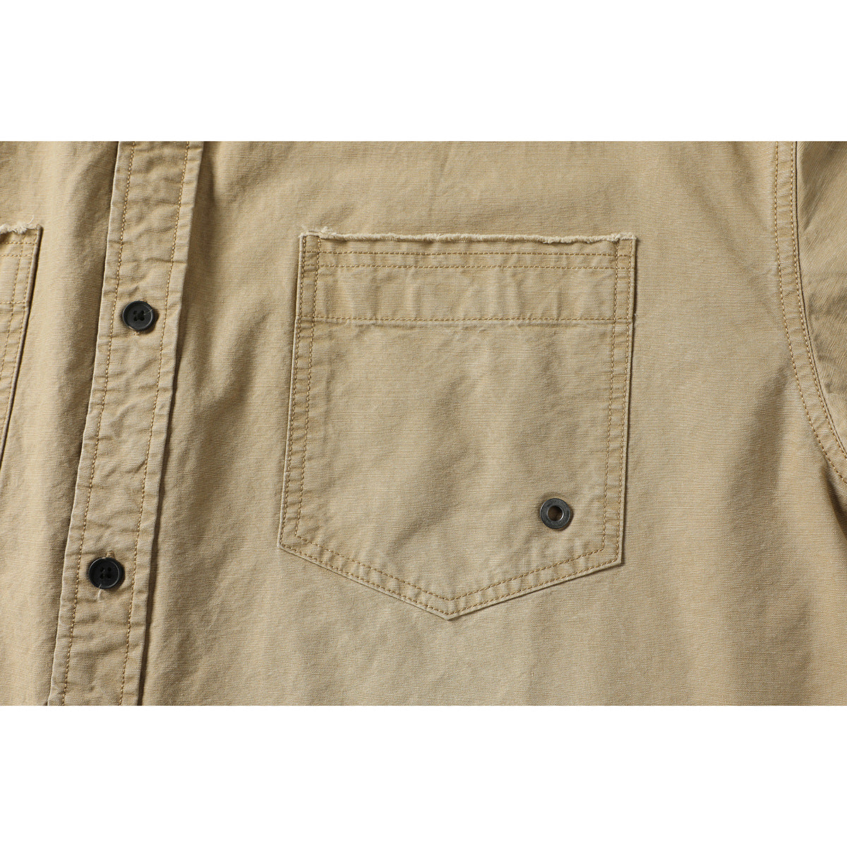 Close-up of a tan shirt’s stitched chest pocket with a small metal eyelet and black front buttons.