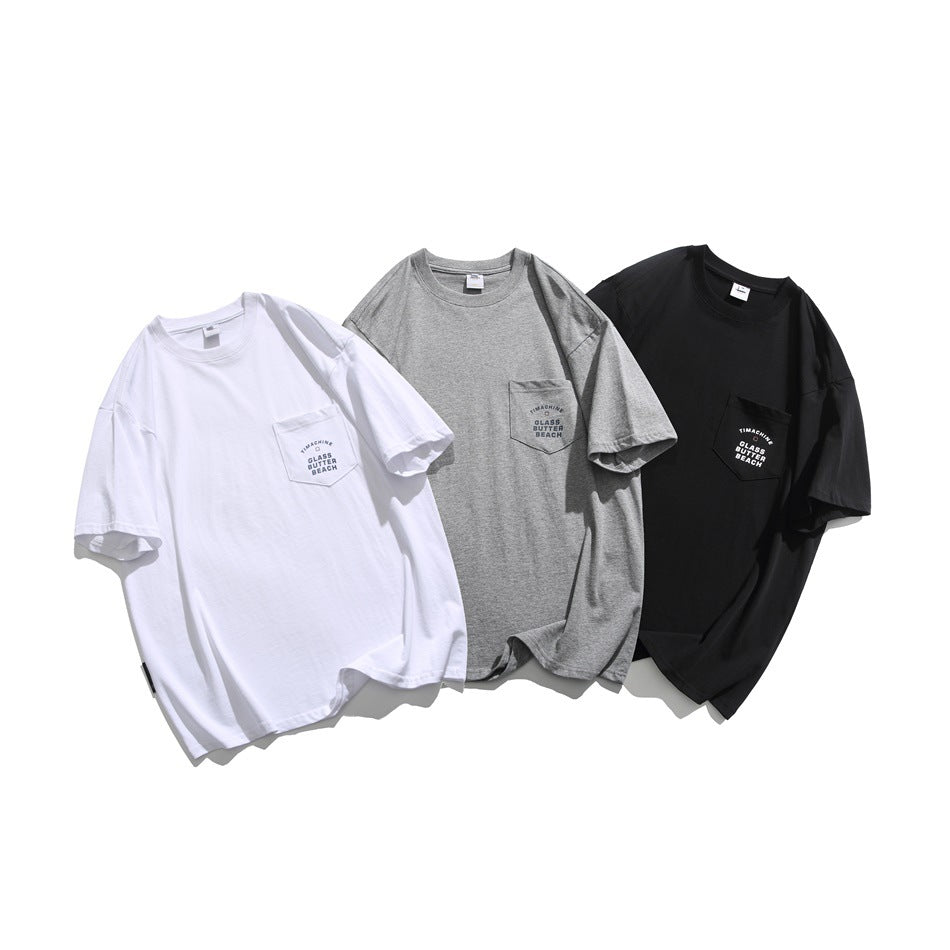 Three oversized short-sleeve pocket T-shirts in white, heather gray, and black, each with printed pocket lettering.