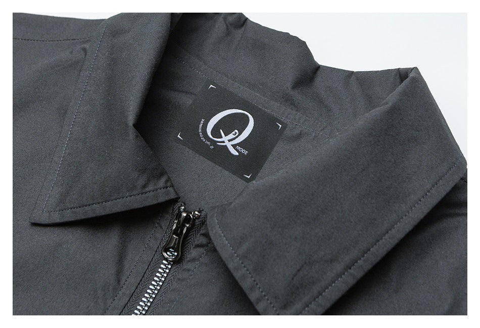 Close-up of a dark jacket's pointed collar, inner neck label, stitching, and metal zipper.