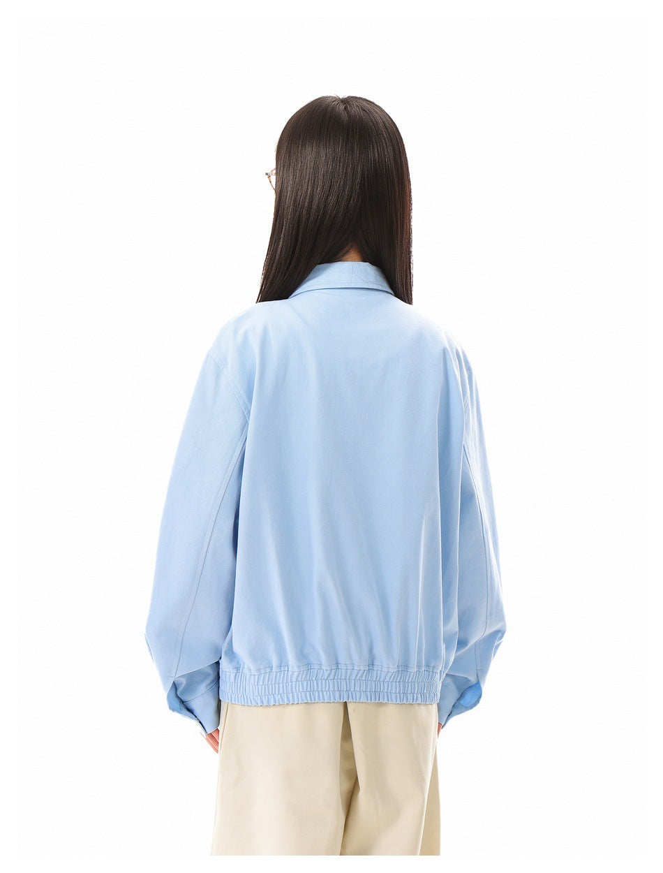 Rear view of a person wearing a light blue jacket with a gathered hem and beige trousers.