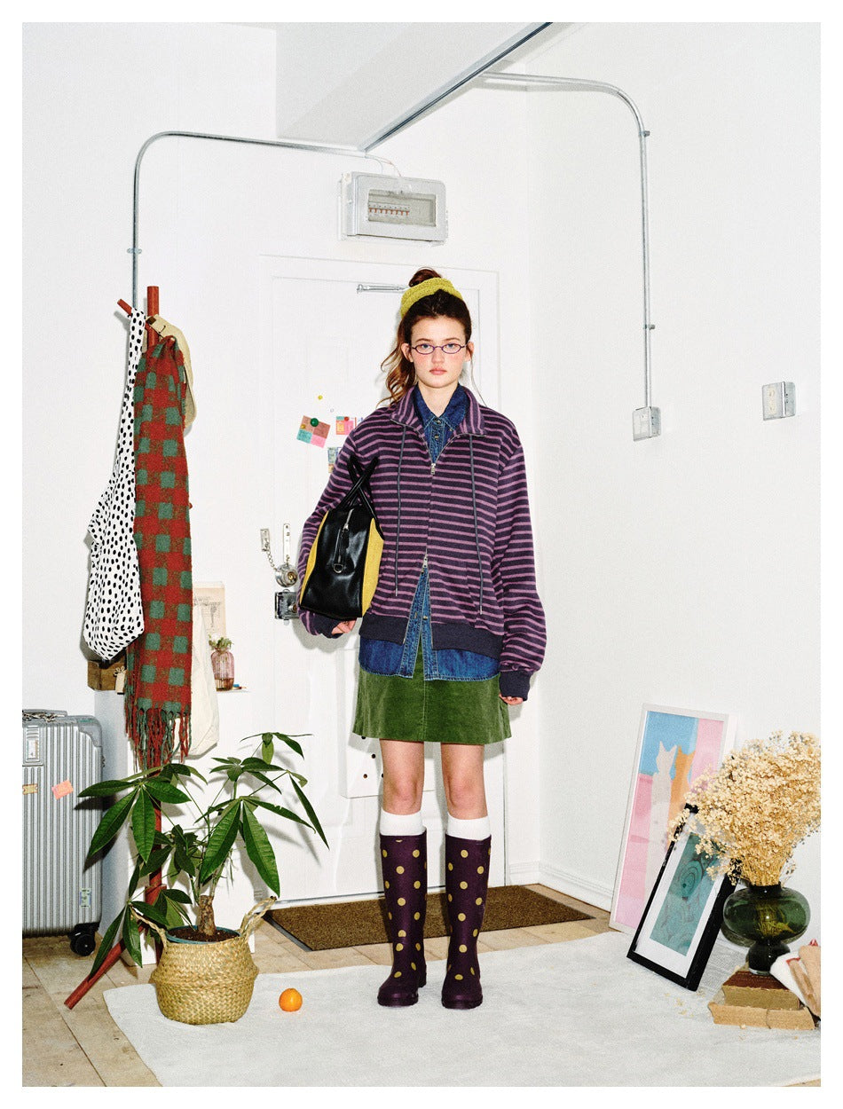 Front view of a model wearing a purple-and-black striped zip jacket over a denim shirt and green skirt.