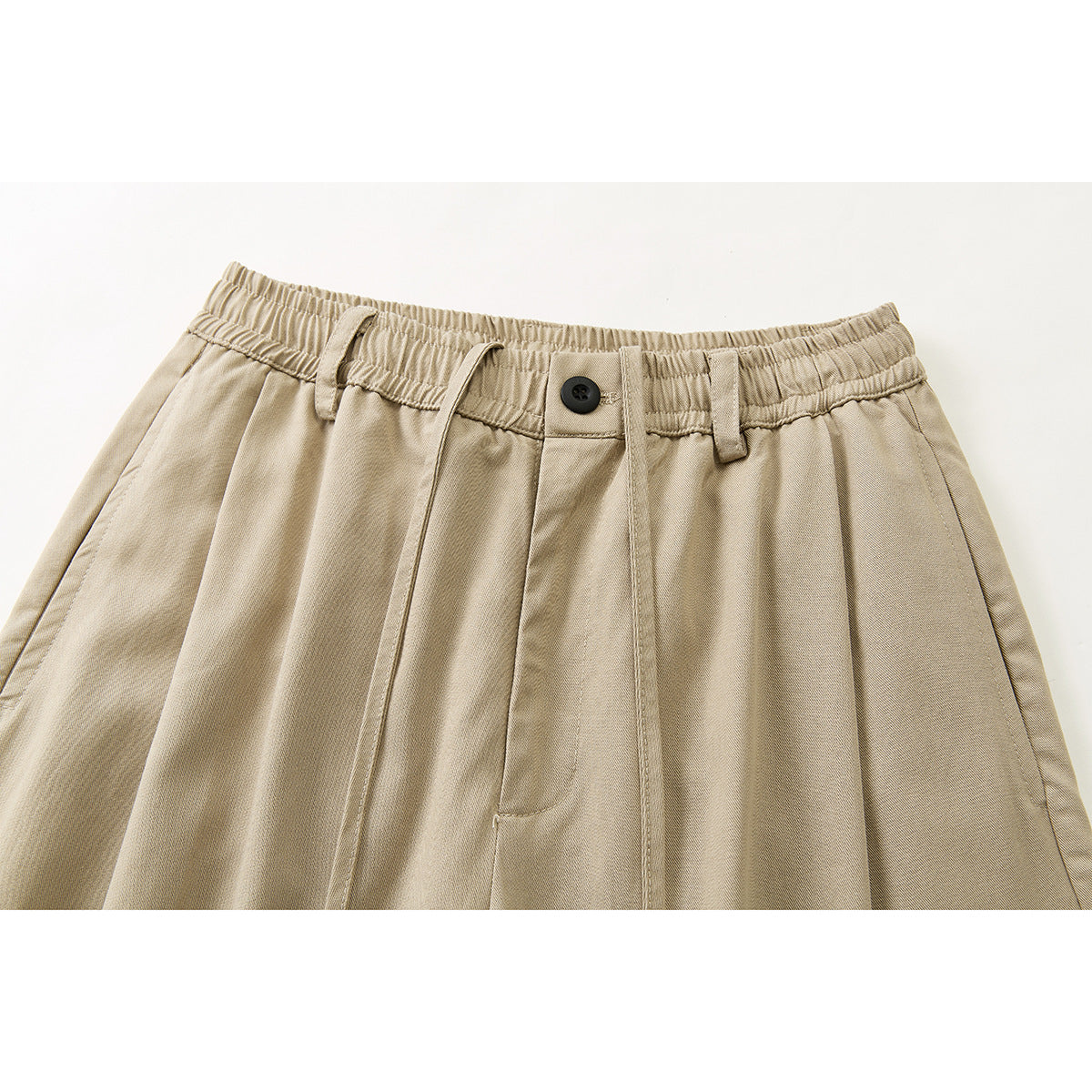 Close-up of beige trousers showing an elastic waistband, black button, belt loops, drawstrings and front pleats.