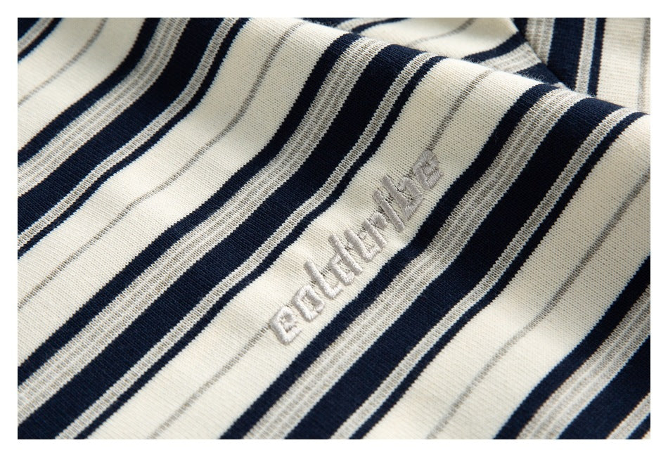 Close-up of small raised script embroidery on cream fabric with navy and gray stripes.