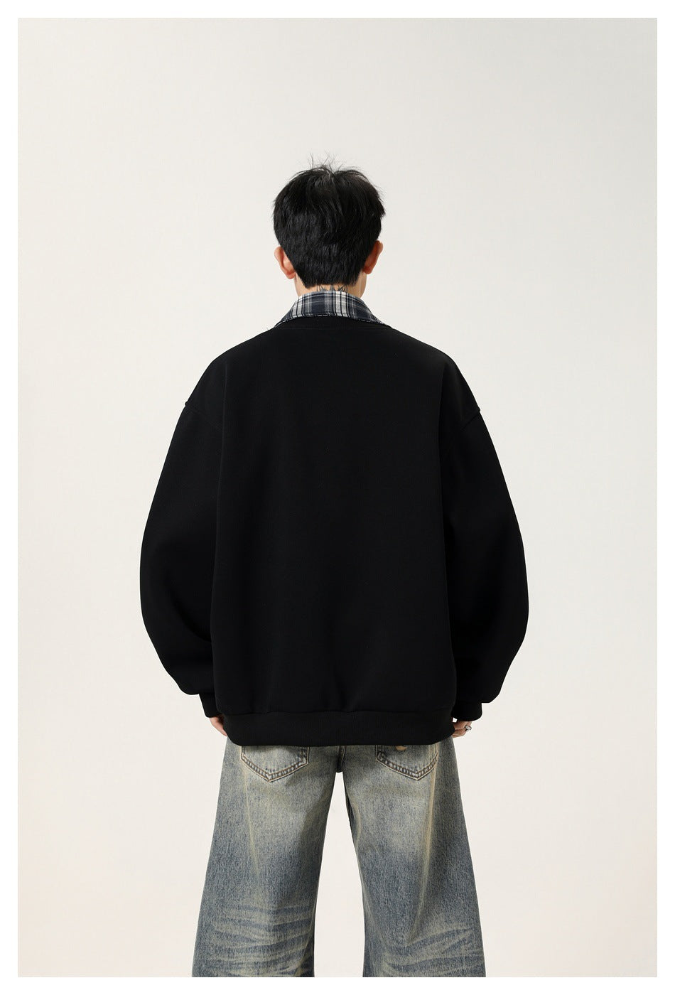 Back view of a model wearing an oversized black jacket with a plaid collar.