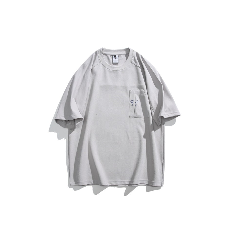 Front view of a light gray oversized T-shirt with a chest pocket and small dark lettering.