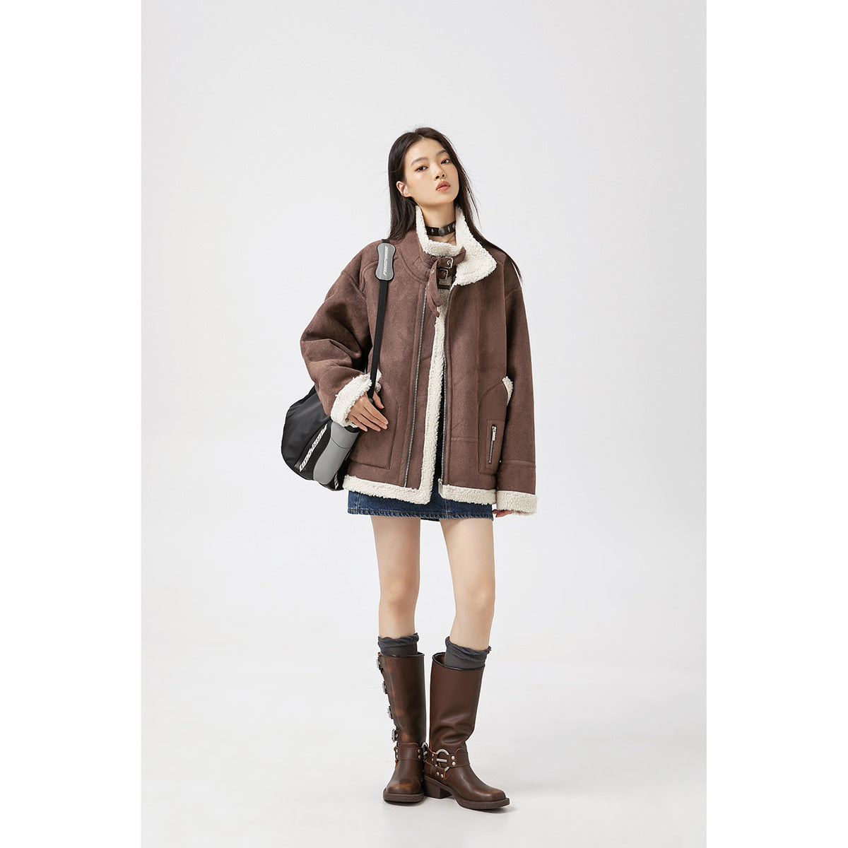 Model wearing an oversized brown jacket with cream fleece trim, asymmetrical zip, buckle collar and patch pockets.
