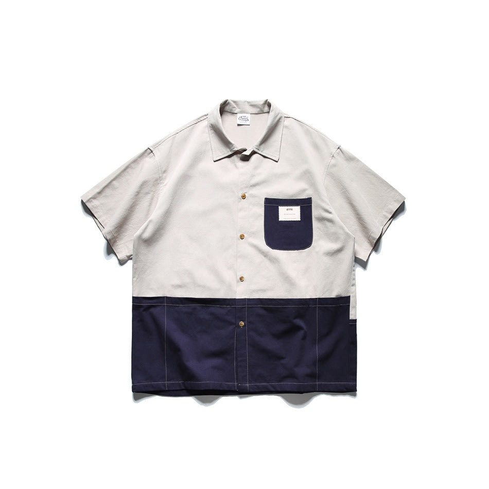 Short-sleeve button-front shirt with a light beige upper and navy lower panel and navy chest pocket, flat lay