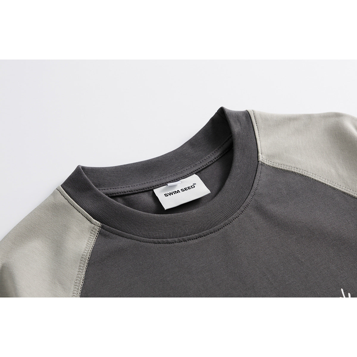 Close-up of a charcoal T-shirt's ribbed crew neck and light gray raglan shoulder seams, with a sewn neck label.