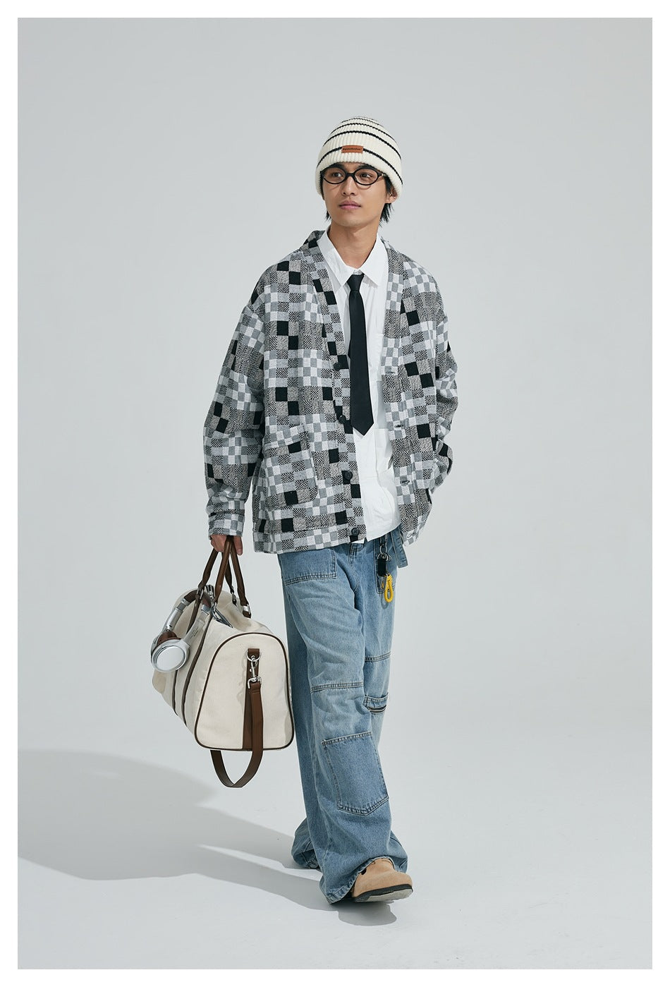 Model walking in a black, gray and white patchwork-check cardigan with blue jeans and a striped beanie.