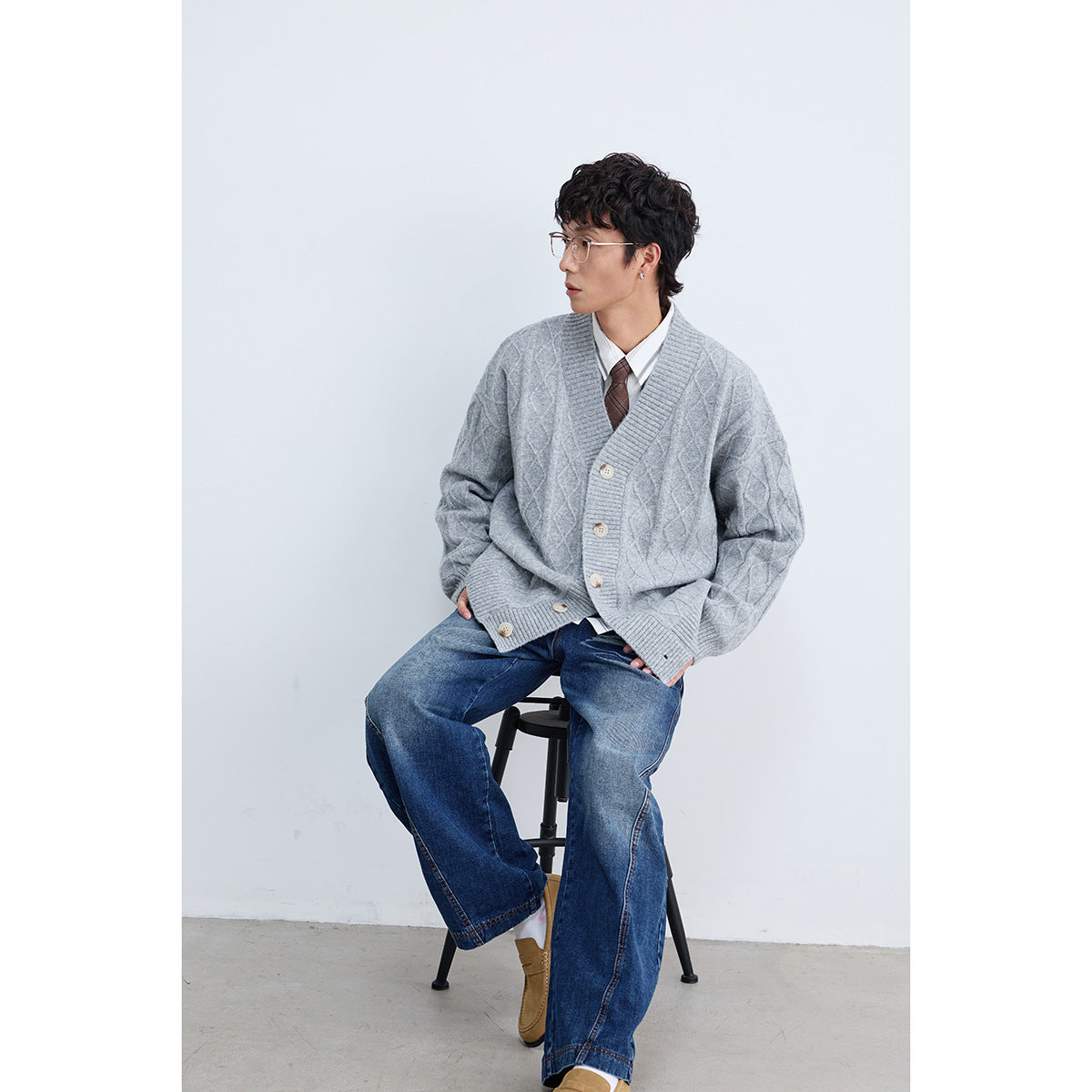 Seated model wearing a light gray diamond-knit cardigan over a white shirt and tie.