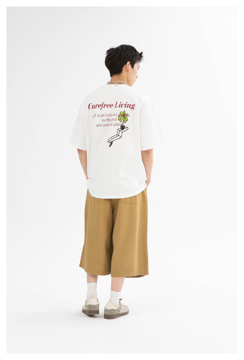 Back view of a model wearing khaki wide-leg knee-length shorts with a white graphic T-shirt and sneakers