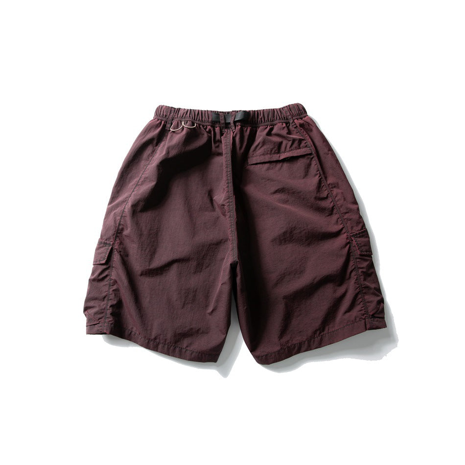 Rear view of deep burgundy cargo shorts with an elastic waist, black webbing belt, and side flap pockets.