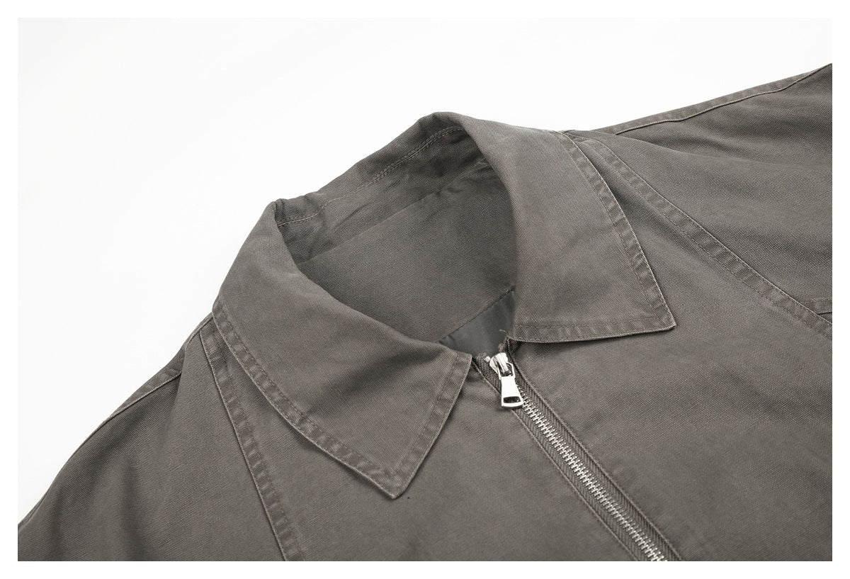 Close-up of a charcoal-gray garment's pointed collar, shoulder seam, and silver front zipper.