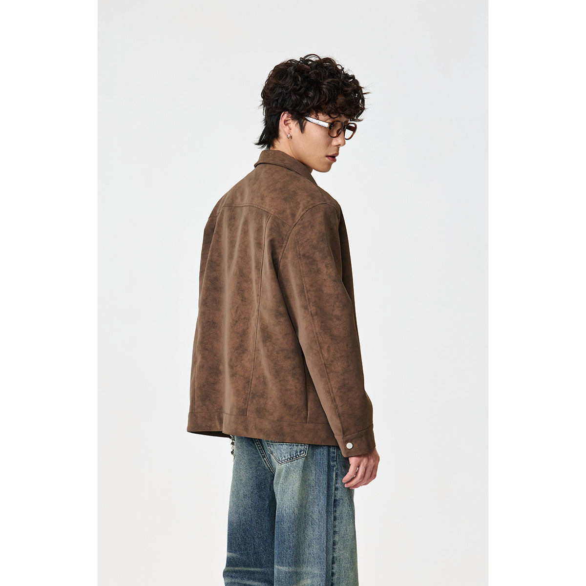 Side-back view of a model wearing a brown jacket with a seam across the shoulders and blue jeans.