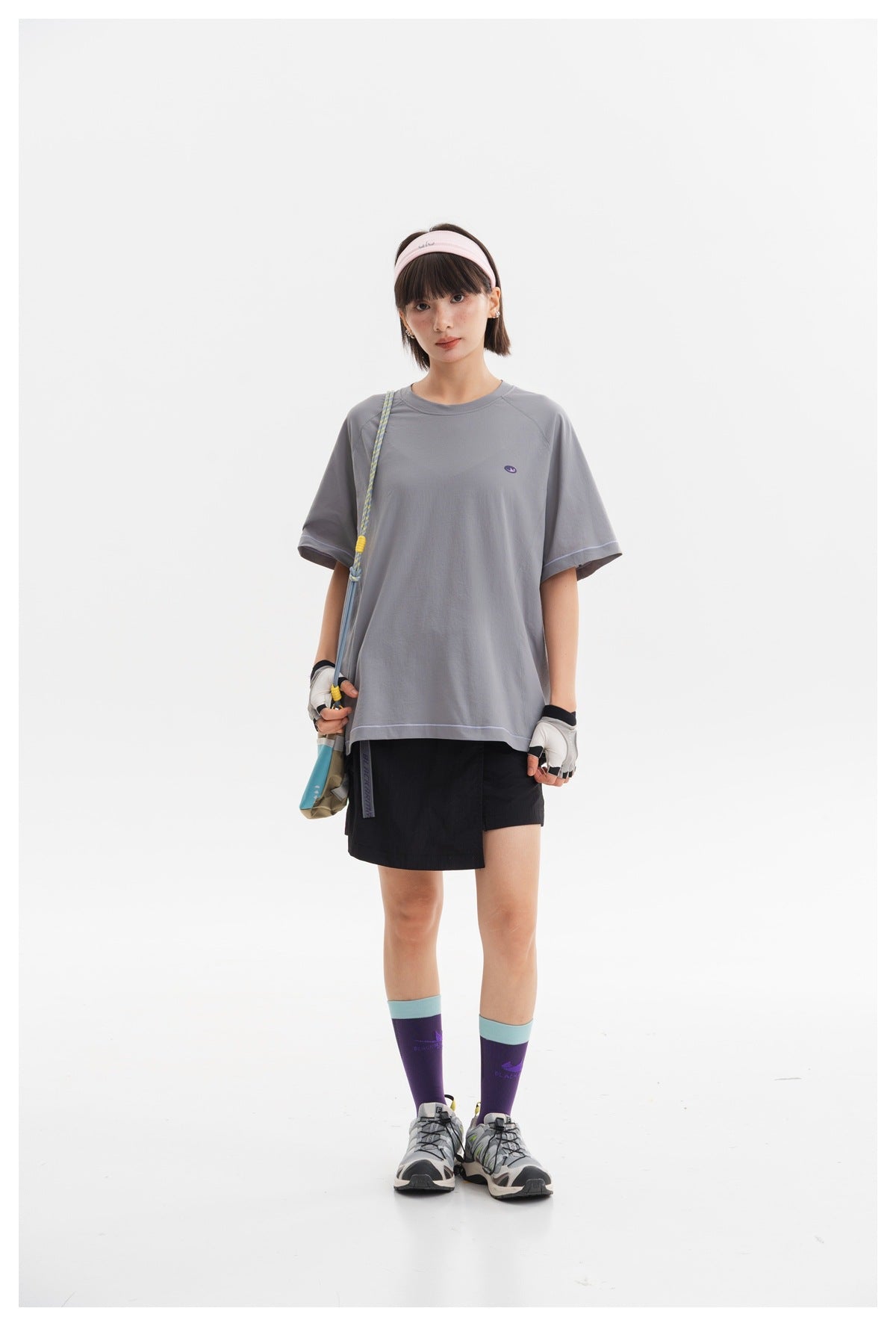 Model wearing an oversized gray T-shirt with black shorts, a crossbody pouch and sporty accessories.