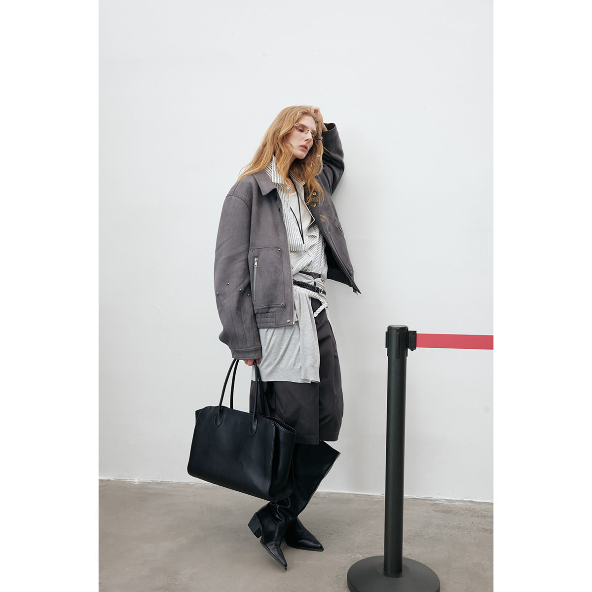 Model wearing a charcoal gray studded zip-front jacket with large pockets, layered over neutral clothes.