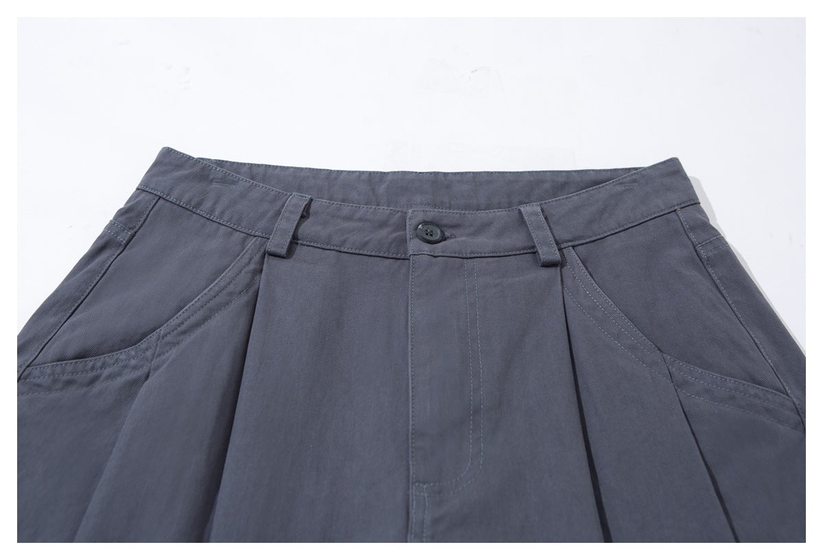 Close-up of charcoal-gray trousers showing the buttoned waistband, belt loops, pleats, and slanted front pockets.