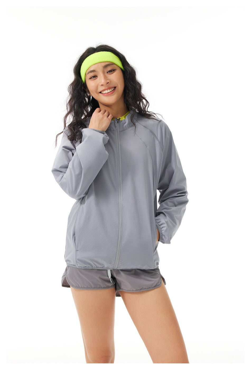 Closer view of a model wearing a light gray zip jacket and matching shorts with a neon yellow headband.