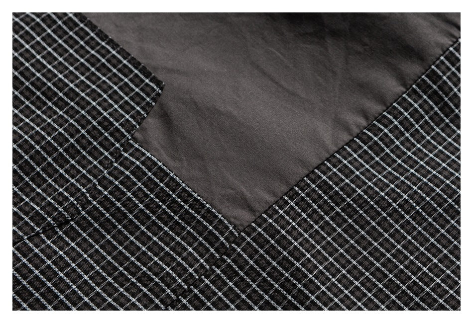Close-up of black fabric with a fine white grid pattern beside a solid charcoal panel and stitched seam.