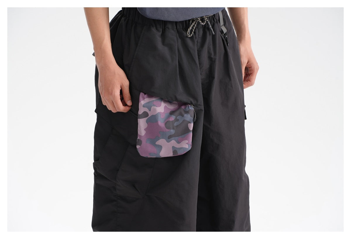 Close-up of black cargo pants showing a pink, gray, and black camouflage-print pocket and drawstring waist.