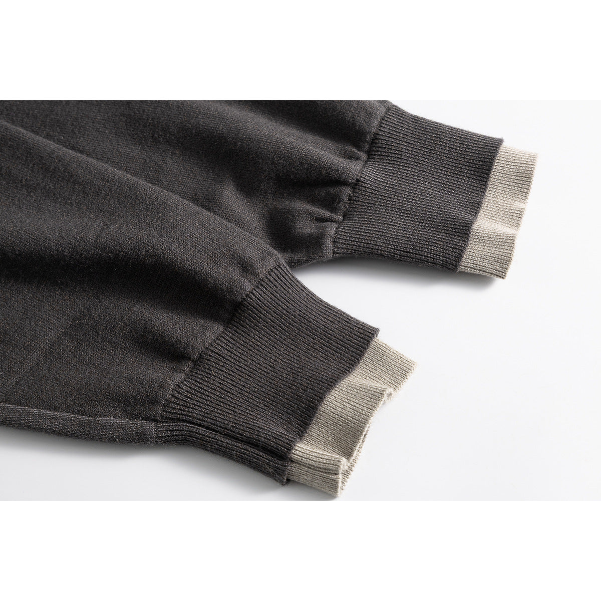 Close-up of charcoal sweater sleeves with wide ribbed cuffs and contrasting beige knit edges.