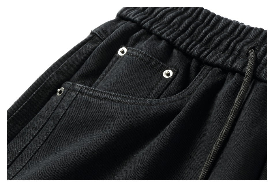 Close-up of the front pocket area on black pants, with a smaller riveted pocket and black waist drawstring.