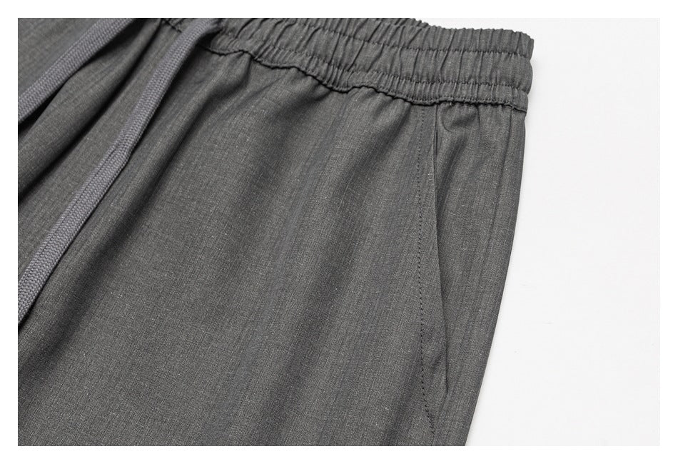 Close-up of dark gray trousers showing a gathered elastic waistband and matching drawstring.