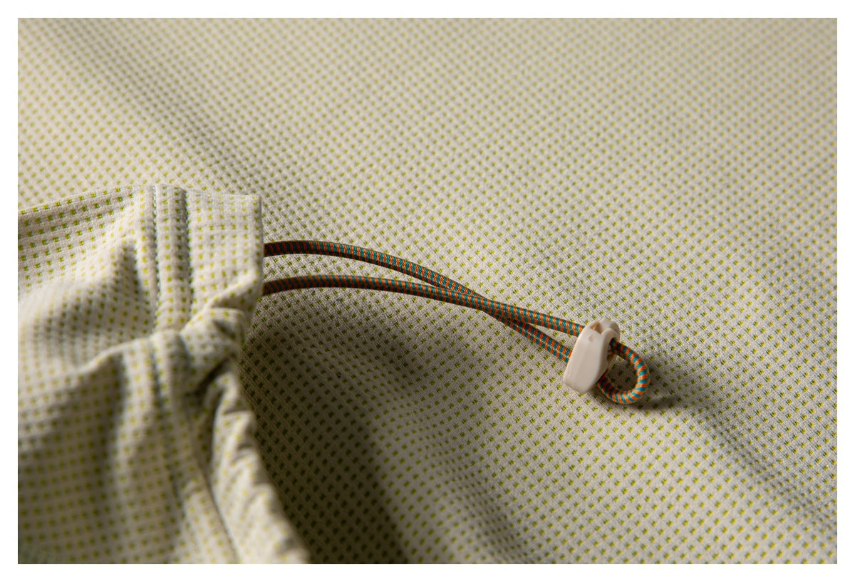 Close-up of off-white fabric with a tiny yellow-green dot pattern and a multicolored drawcord with a pale toggle.