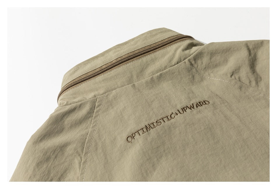 Close-up of khaki fabric with a zipper and embroidered “OPTIMISTIC UPWARD” text.